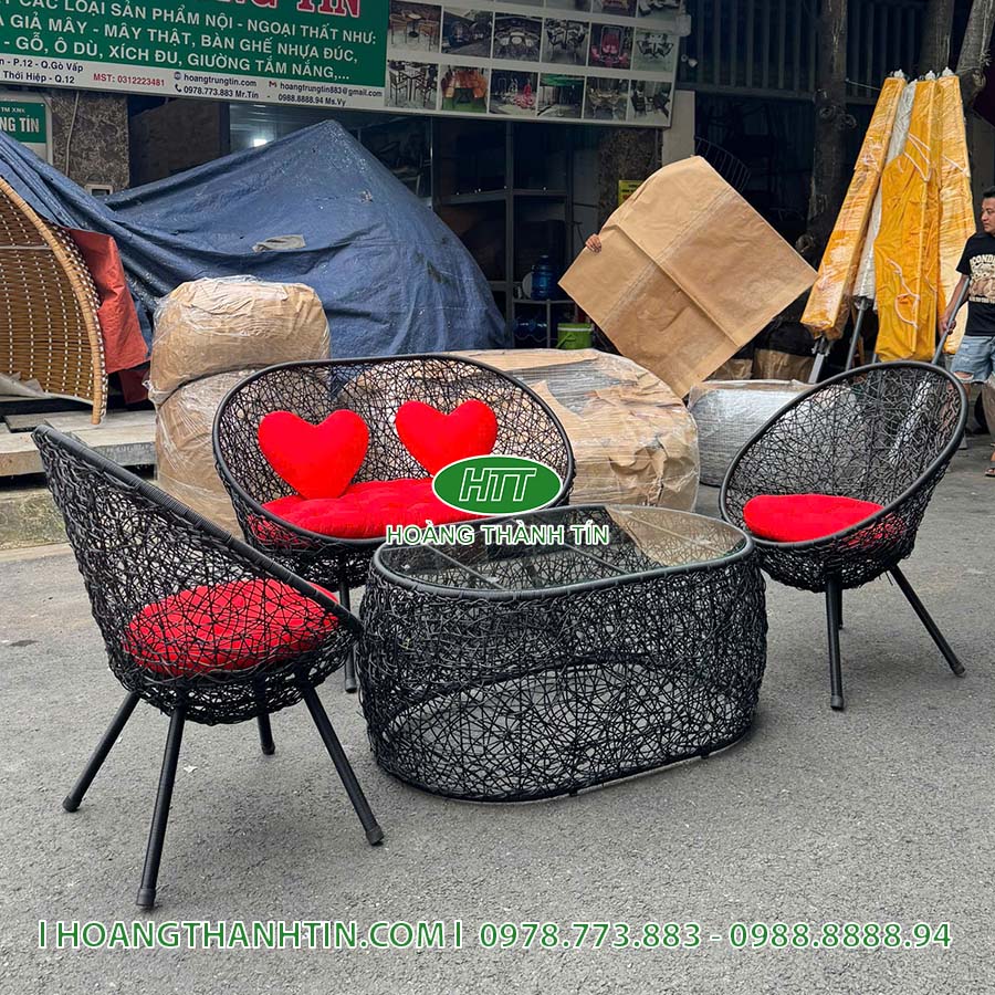 Bộ bàn ghế HTT 1 nhìn gần - ghế băng đôi đan sợi đen với hai gối tim đỏ, bàn mặt kính bầu dục