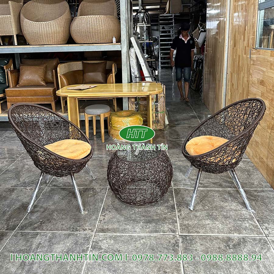 Bộ bàn ghế HTT 2 đặt trong showroom - hai ghế nâu nệm vàng cam quanh bàn đan tròn, chân inox sáng bóng