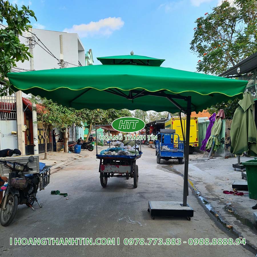 D&ugrave; che nắng vu&ocirc;ng m&agrave;u xanh l&aacute; đậm k&ecirc; trước qu&aacute;n tr&ecirc;n vỉa h&egrave; c&oacute; xe cộ qua lại